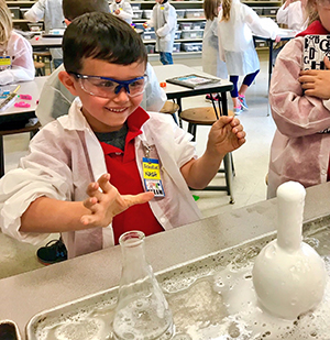 Boy delighted by beaker bubbling over for website.jpg Boy delighted by beaker bubbling over in science class